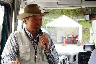 バスの運転席近くで帽子をかぶった小野寺先生がマイクを持って話している様子をアップで撮影した写真