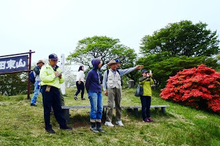 展望台の広場で数人の参加者が立っており、小野寺先生が遠くを指さして説明している写真