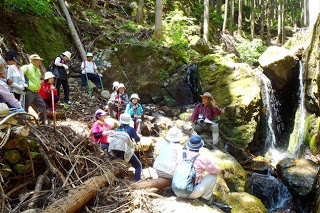 参加者たちやガイドの男性が、小さな滝がある大きな岩場付近にが座って休憩している様子の写真