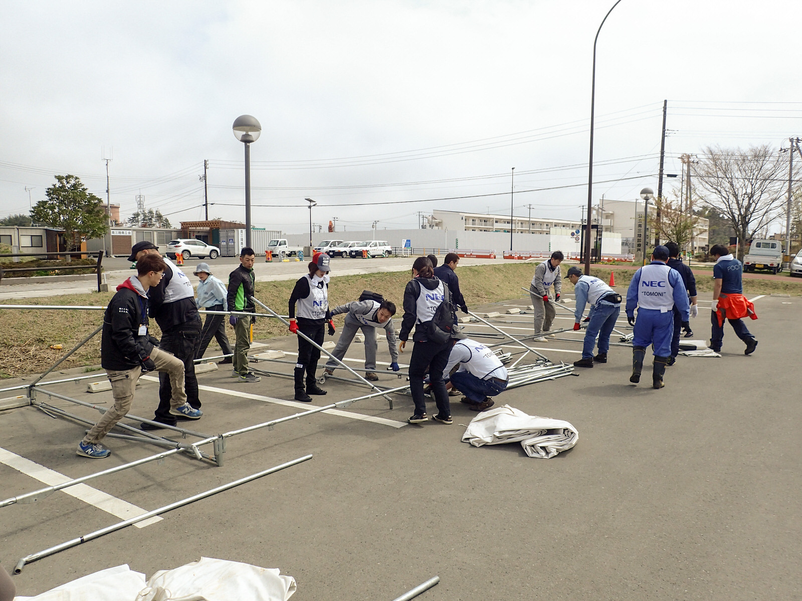 駐車場に集まった出店者・ボランティアの方々が、テントの骨組みを組み立てている様子の写真