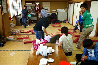 畳の部屋に長机と赤い座布団が広げられ、子どもと大人が自由に動き回って遊んだりくつろいだりしている様子の写真