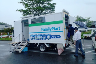 「FamilyMart」のロゴと「移動販売車ファミマ号」と書かれた白いトラック型の移動販売車が駐車場に停まり、階段を使って男性が中へ入ろうとしている写真