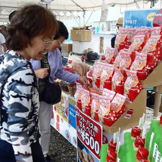 赤いパッケージのおせんべいがたくさん陳列されており、女性たちが笑顔で手に取って商品を見ている様子を写した写真