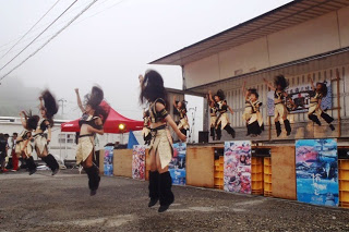 ステージ前の広場で、揃いの衣装を着た地元のダンスチームが勢いよくジャンプしてダンスを披露している様子の写真