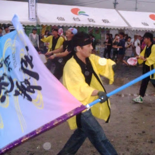 黒い鉢巻を巻いた若い男性が、黄色い法被姿で力強く大きな旗を振っている様子をとらえた写真