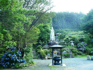 紫陽花が咲く緑豊かな山間の庭園に、石段の上に白い観音像が立ち、手前には香炉と灯籠が置かれている徳性寺庭の写真