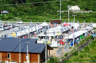 駐車場の一角に設けられた白いテントが立ち並ぶ仮設商店街に多くの人が訪れて買い物や交流を楽しんでいる八幡川かがり火まつり福興市の様子の写真