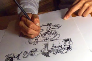 黒インクで細かい模様を組み合わせた独特なスタイルのイラストを紙に描いている途中の手元をアップで撮影した写真