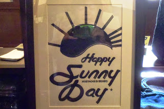 黒い太陽のようなモチーフの下に「Happy Sunny Day」という文字がデザインされ、額縁に入れられて展示されているイラスト作品の写真