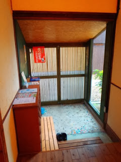 引き戸の格子扉、床が特徴の日本の伝統的な玄関のつくりで、靴箱があり、抜いた靴がそろえて置かれている玄関の内側の写真