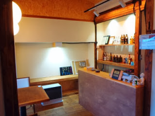 木製のカウンターと棚に酒瓶が並び、照明の光で温かみのある室内の受付カウンターの写真