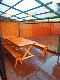 半透明の波板屋根とオレンジ色のパーティションに囲まれ、木製の長机とベンチが並べられた屋外テラス席の写真