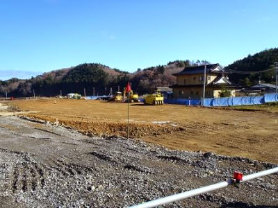 手前に配管資材が写り、その奥に整地作業中の平地と建物が見え、工事中の様子がわかる西戸地区の災害公営住宅造成地の写真