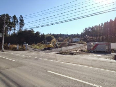 道路の向かい側でショベルカーなどの重機が作業中で、森林に囲まれた土地が造成されている様子が写された波伝谷団地の工事現場の写真