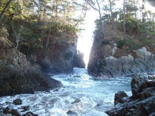 海から押し寄せる波が両側を岩に挟まれた狭い割れ目を勢いよく通り抜けている様子で、割れ目の奥にはまぶしい光が差し込んでいる写真