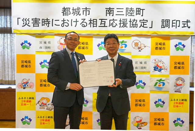 バックパネルの前で都城市長と南三陸町長が協定書を一緒に持っている写真