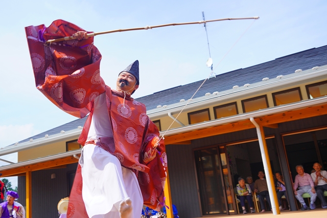 赤い衣装の男性が屋外ステージで棒を使って演技している写真