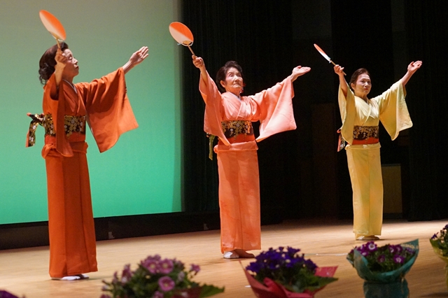 舞台の上で和服を着た三人の女性が扇子を持って優雅に踊っている写真