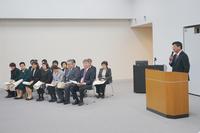 演台に立っ町長がマイクを使って話しており、向かい側には賞状を手にした複数の男女が椅子に座って静かに耳を傾けている写真