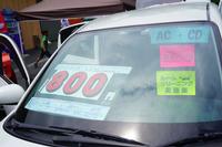 白い車のフロントガラスに「800」と大きく書かれた価格表示や、装備や情報が書かれたカラフルな紙が貼られており、中古車が販売されている様子を示す写真