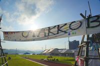 青空の下、手作り感のある木の支柱に布を渡したゲートに「UTAKKO BURUME」と描かれており、その先にテントや建物が並ぶ会場の様子が見えるイベント会場の写真