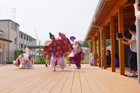 釣り竿や鯛の模型などを持った赤や紫の衣装を着た複数の人が屋外ステージで演舞している写真
