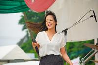 ステージの前で、白いシャツを着た女性がマイクを持って笑顔で歌っている、女性ボーカルによるステージパフォーマンスの写真