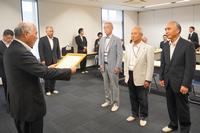 感謝状を読み上げる男性の前に、数人の男性たちが真剣な表情で整列して立っている写真