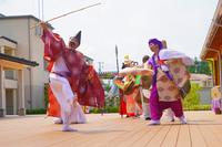 赤い装束の人物が竹製の釣り竿を振り上げ、周囲の仲間とともに舞っている写真