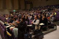 観客席に多くの人が座り、ステージを見ながら拍手をしている様子の写真