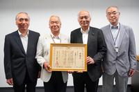 感謝状を手にした男性を中心に、スーツ姿の4人の男性が並んで笑顔を見せている写真