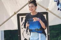 ステージ上で、髪はお団子でまとめられている黒いTシャツを着た女性がマイクを持って歌っている、女性ボーカルのライブ中の写真