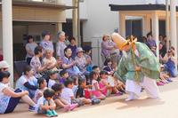 緑の衣装を着た人物が前列の子どもたちと笑顔でふれあっている写真