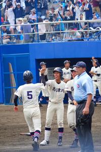 ホームベース付近に集まった白いユニフォームの選手たちが喜びながらハイタッチを交わし、背後の観客席では大勢の観客が立ち上がって青い応援グッズを振って声援を送っている活気あふれる様子の写真