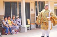 金色の衣装を着た男性が年配の女性たちの前で笑顔を見せている写真