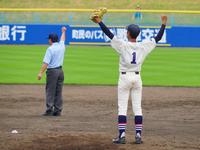 グラウンドで背番号1番の高校野球の選手が両手を高く掲げ、奥では審判がアウトの判定を示している場面の写真