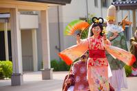 ピンク色の和服を着た女性が扇子を持ち、笑顔で歩いている写真