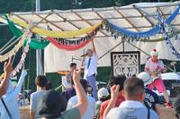 ステージでバンドが演奏しており、観客が手を上げて応えている野外音楽フェスの様子の写真