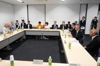 多数の人々がロの字型に配置された会議室のテーブルを囲んで真剣に話し合っている様子の写真