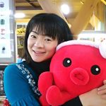 ねじり鉢巻きをしたオクトパス君のぬいぐるみを顔に近づけた、青色の服を着た女性をアップで撮影した写真