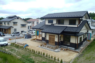 和風の二階建て住宅が完成に近づいており、玄関前に庭や植栽が整えられつつある住宅街の一角の写真