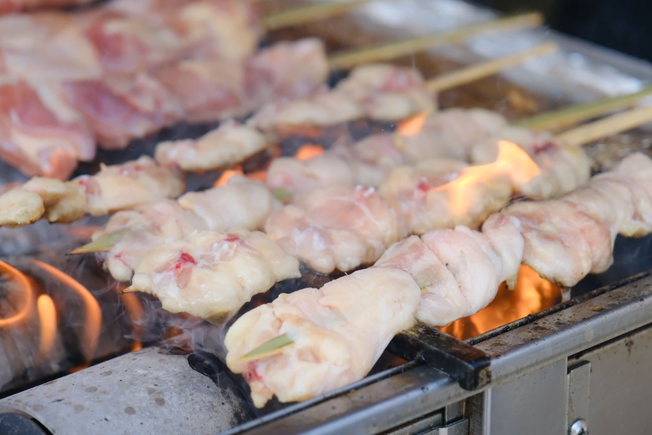 炭火の上で串に刺さった生の鶏肉に炎が上がって焼かれている途中の様子をアップで撮影した写真