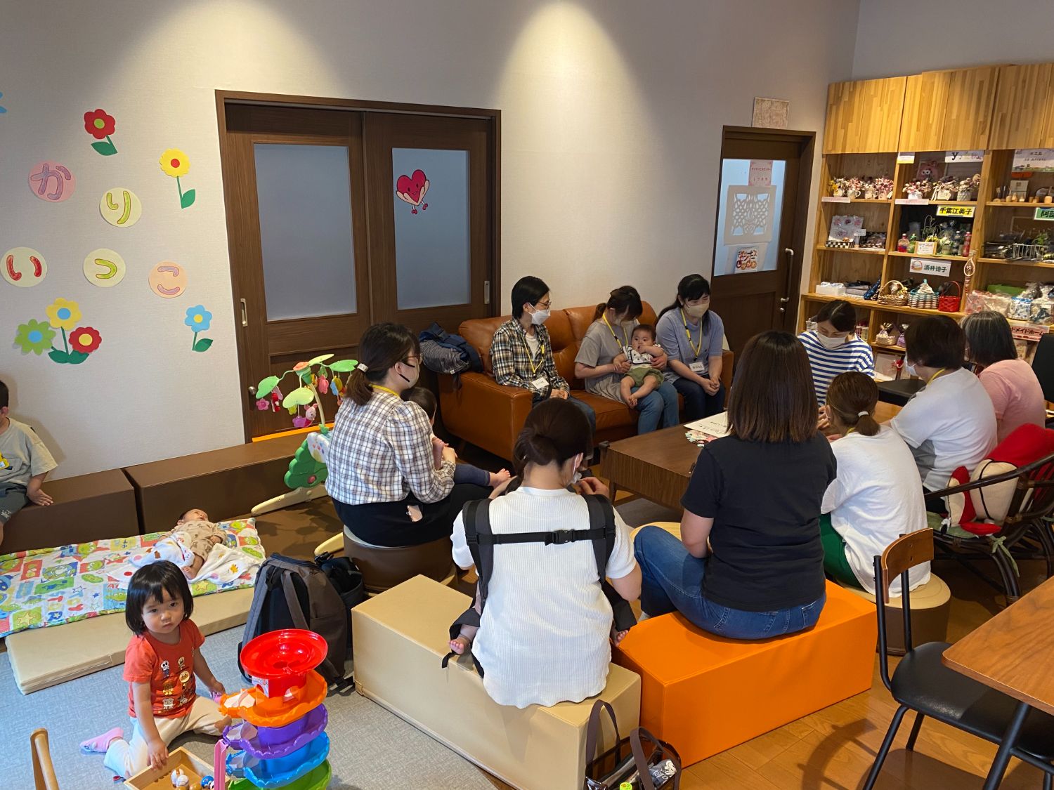 乳児を抱いた母親たちがリラックスした雰囲気で集まり、座って会話をしている様子が見られる「あずかりあいっこ」交流会の写真