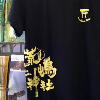 黒いTシャツに金色で「荒嶋神社」と大きく書かれ、胸元には鳥居マークが書かれているデザインTシャツの写真