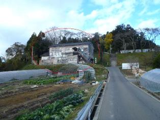 両側に農地が広がる1本道のゆるやかな上り坂の先に、緑の森を背に建つ、南三陸復興ダコの会のYes工房の建物を赤丸で囲んで示した画像