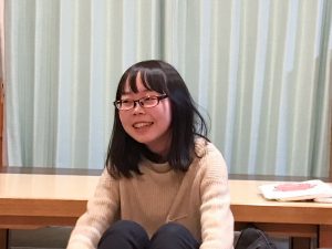 メガネをかけた佐藤知里さんが床に座って笑っている写真
