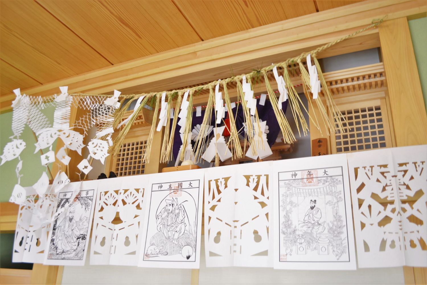 飾りが神棚の上部や横に吊るされ、白い紙の持つ清らかさが神聖な雰囲気を漂わせている様子の写真