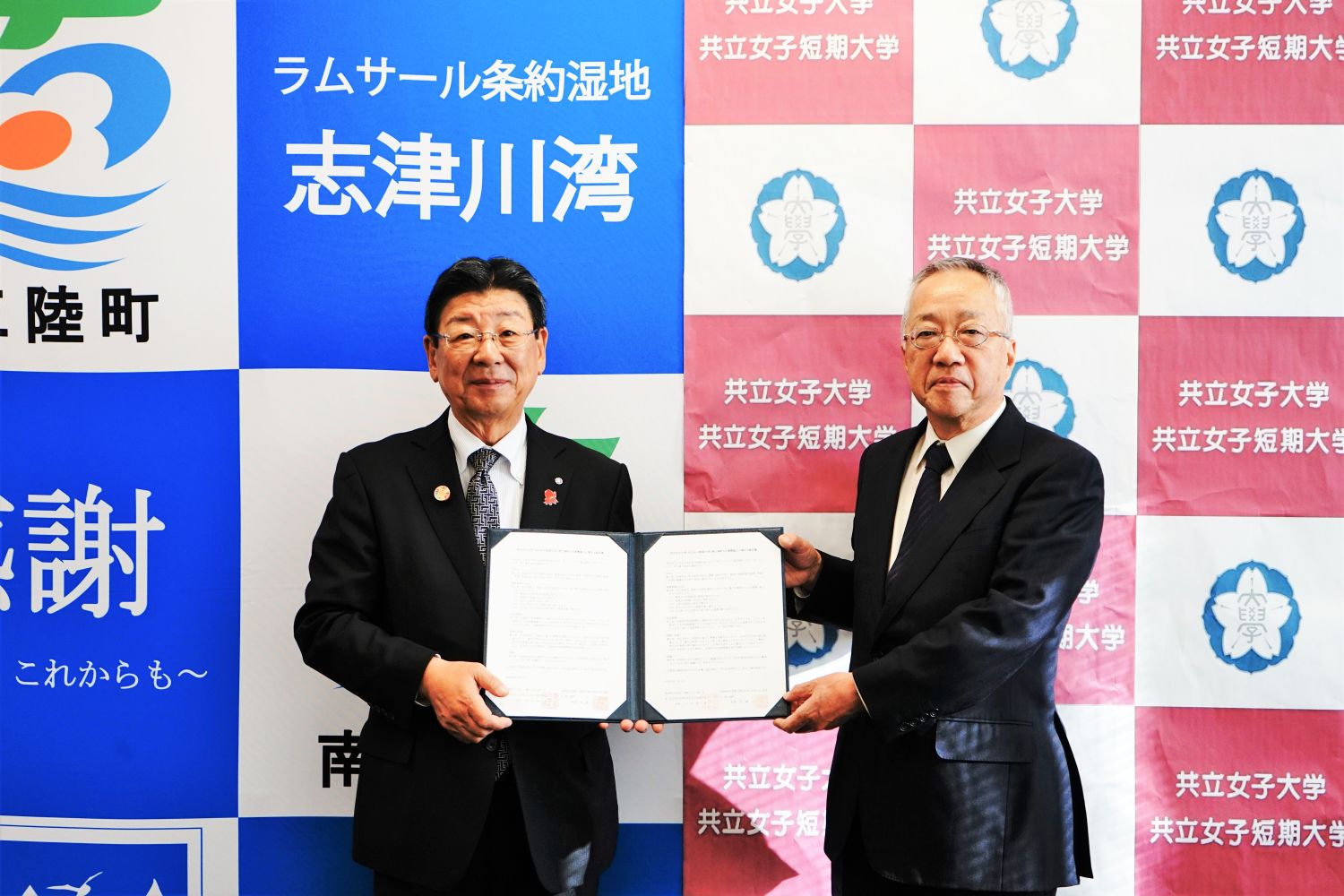 南三陸用のバックパネルの前で、南三陸町の佐藤町長と共立女子大学の村上副学長が並んで立ち、地域連携に関する協定書を一緒に持って並んでいる写真
