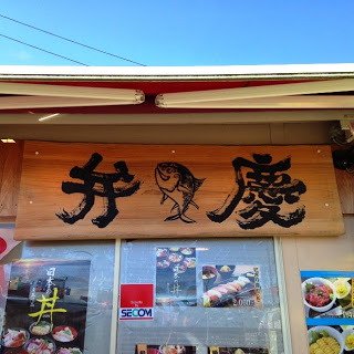 木の看板に「弁慶」という文字と魚のイラストが描かれ、下には海鮮丼などの写真が貼られている食事処の外観の写真