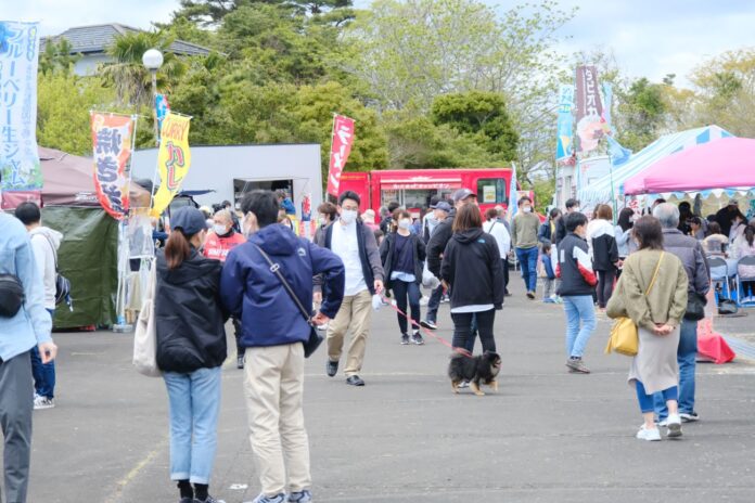 屋台やキッチンカーが並ぶ賑やかな会場で、犬連れの男性や買い物を楽しむ人など多くの人々が歩き回っている、潮騒まつり会場の様子の写真